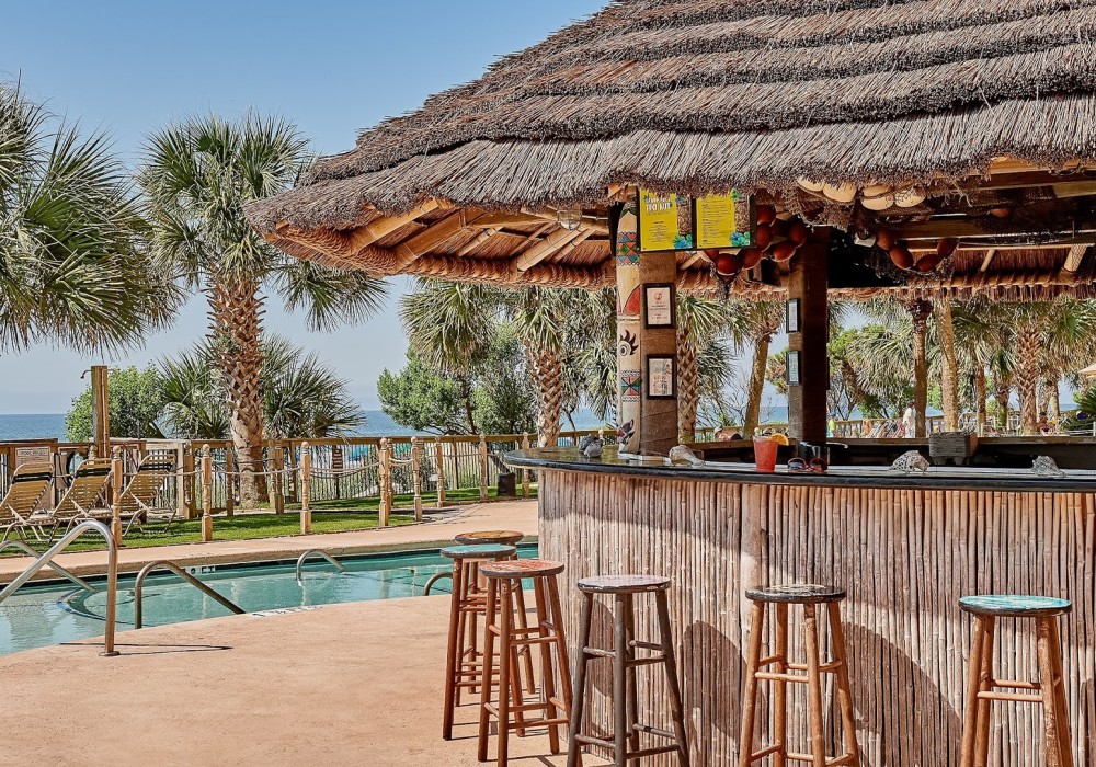 a bar with stools and a pool in the background