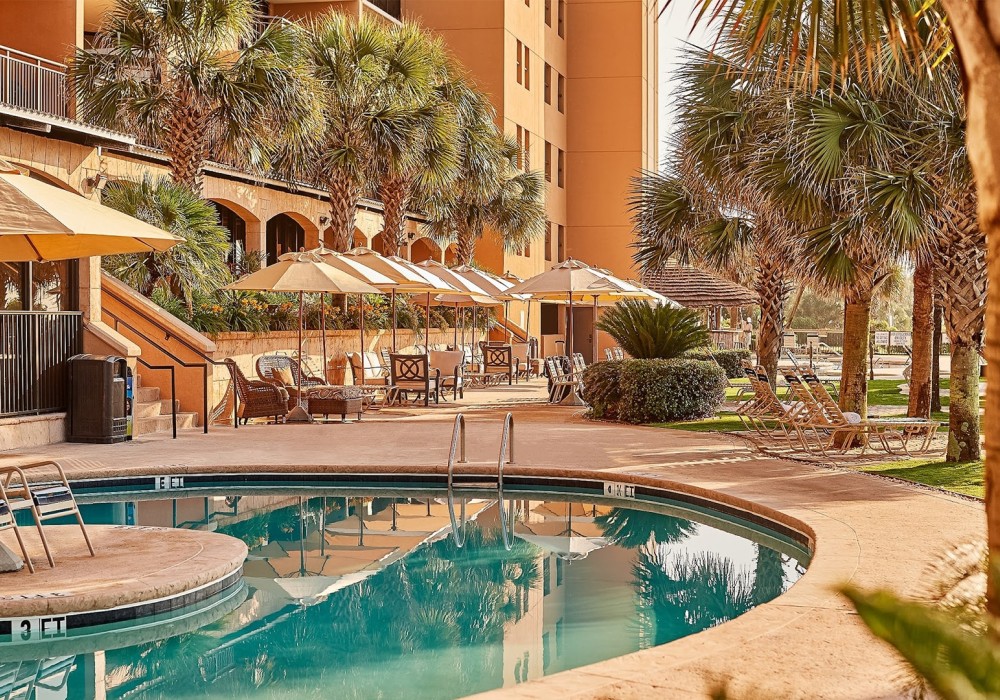 a pool with umbrellas and chairs in front of a building