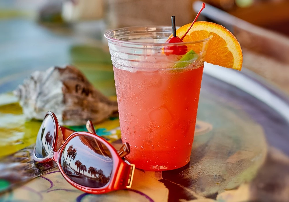 a drink in a plastic cup with a cherry and a slice of orange