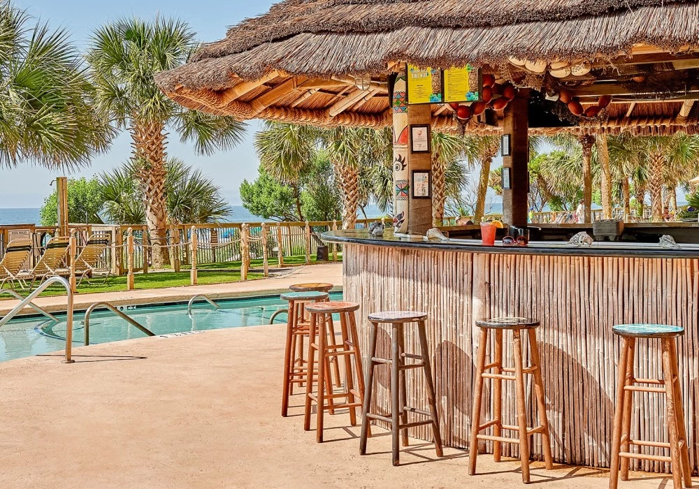 a bar with stools and a pool in the background