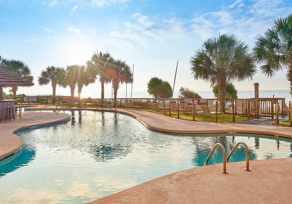 a swimming pool with palm trees and a beach in the background