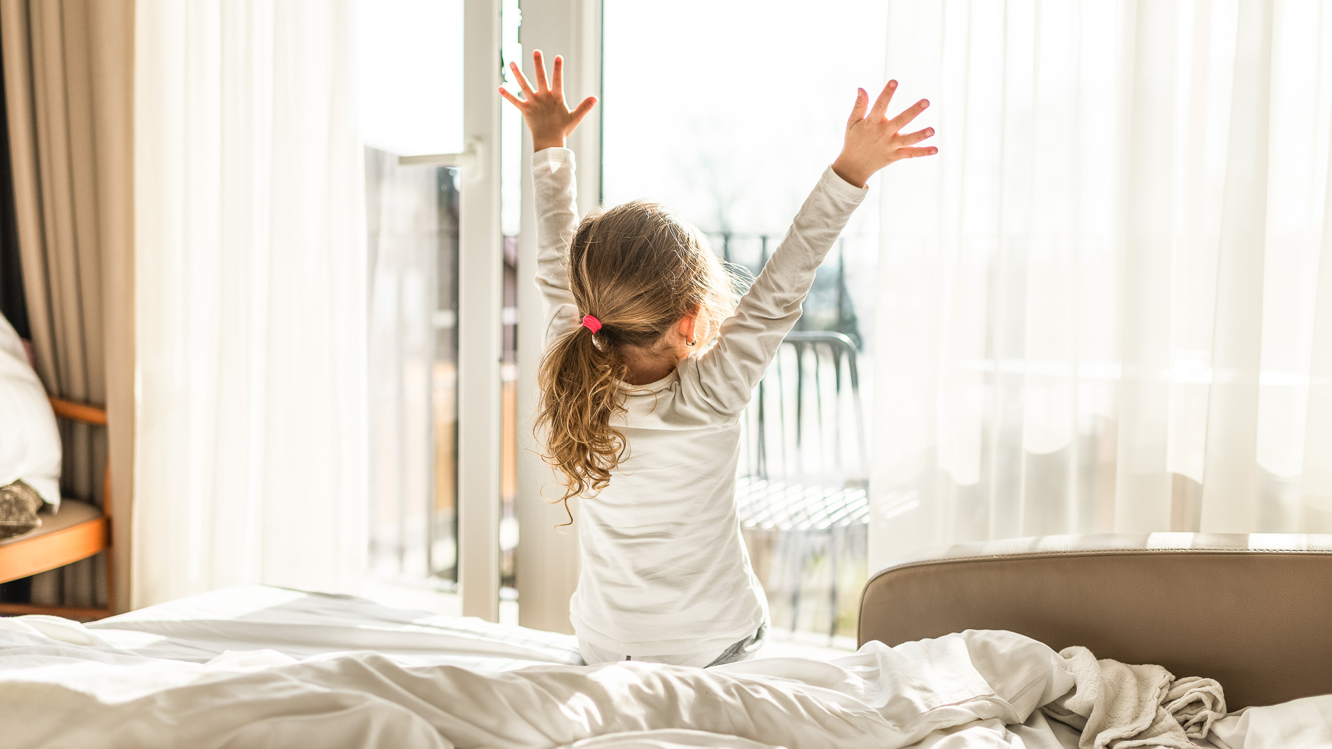 a girl sitting on a bed with her arms up