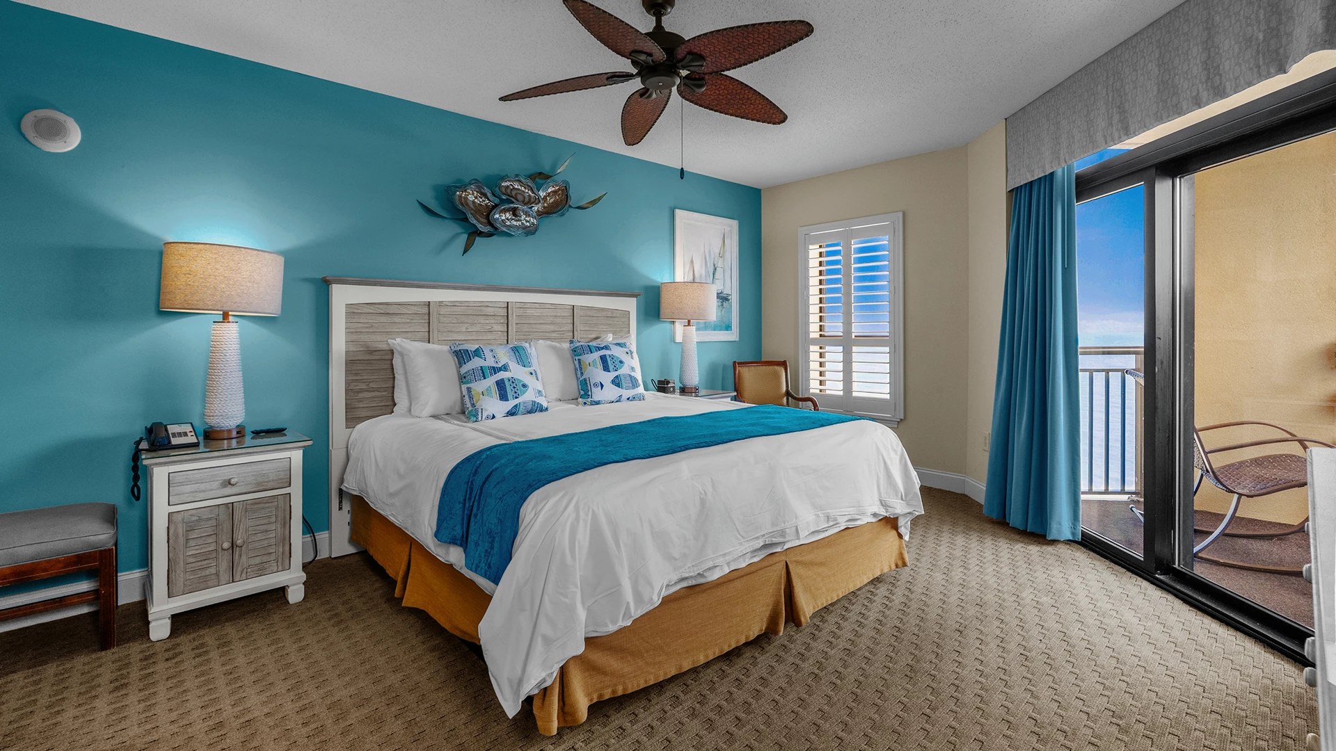 A hotel room with a blue accent wall, white bedding, and a ceiling fan.