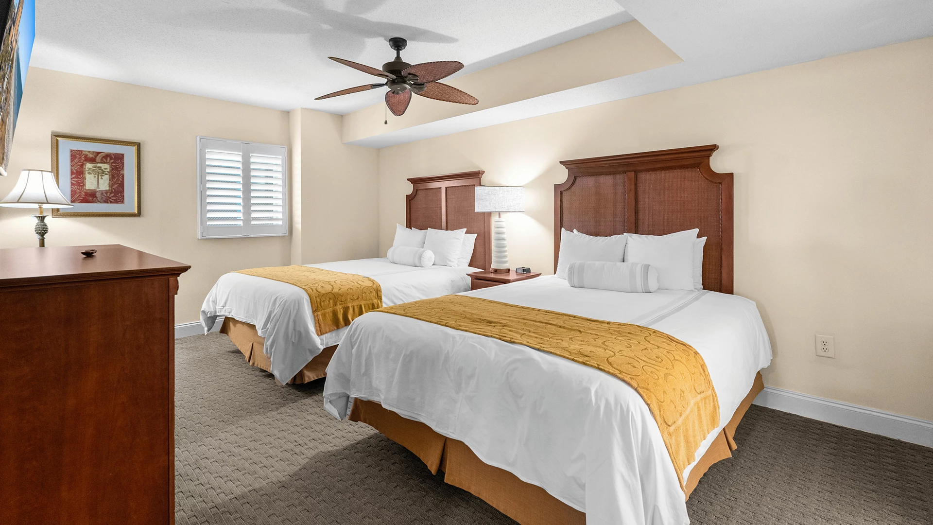 A hotel room with two beds, wooden headboards, and yellow blankets.