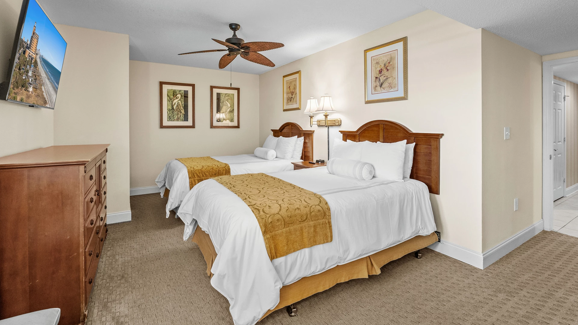 A hotel room with two double beds, a ceiling fan, and a flat-screen TV on a dresser.