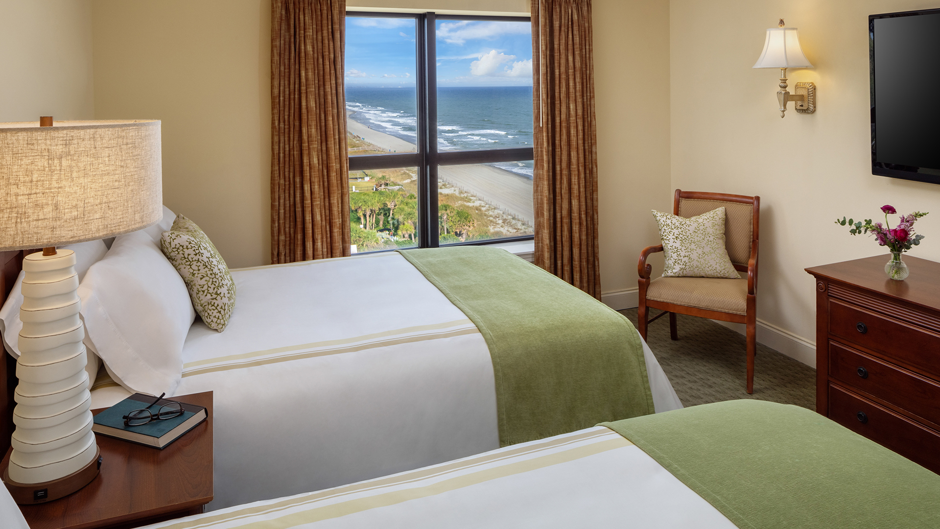 a room with two beds and a chair and a beach view