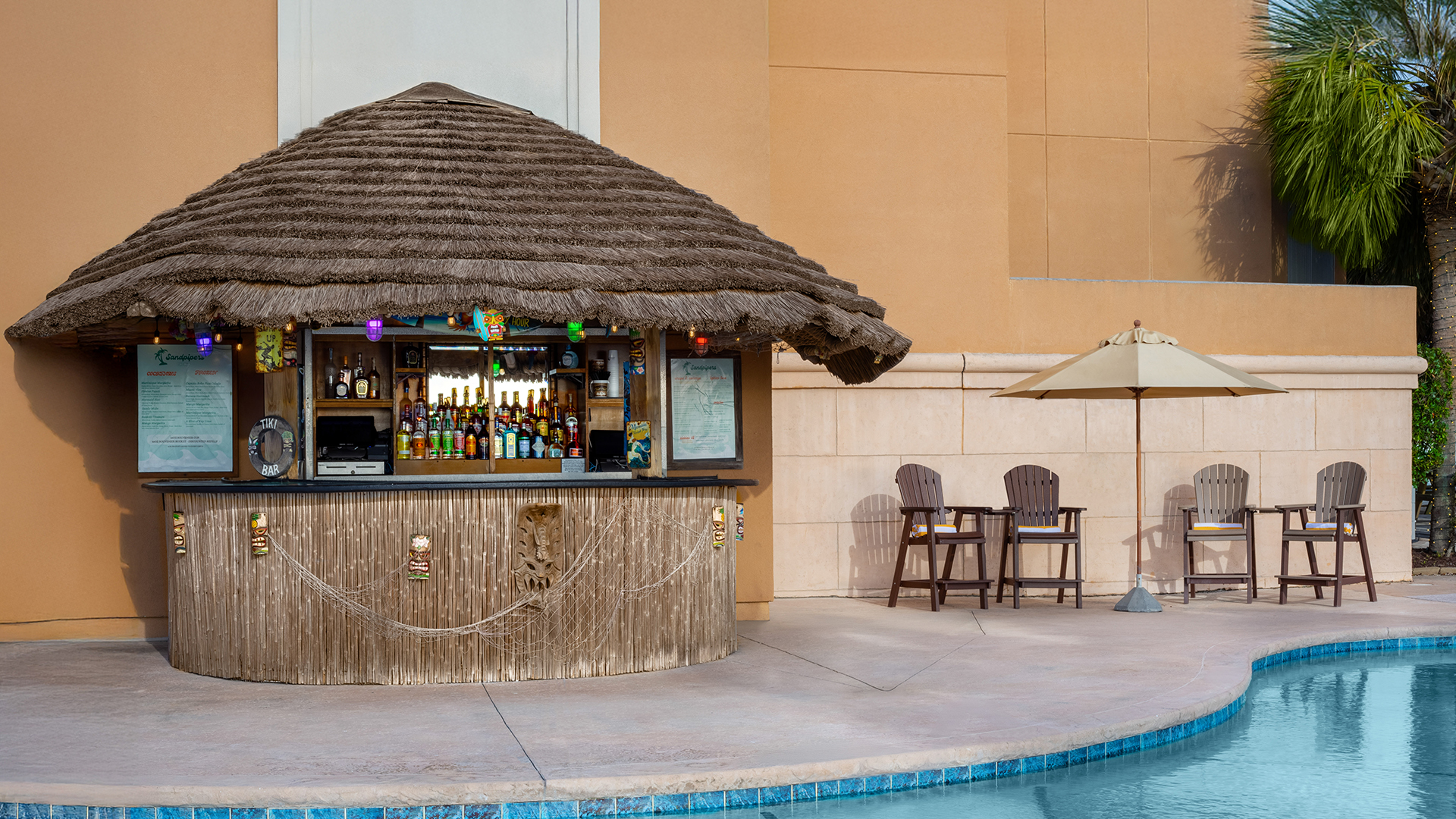 a bar with a straw roof and chairs next to a pool
