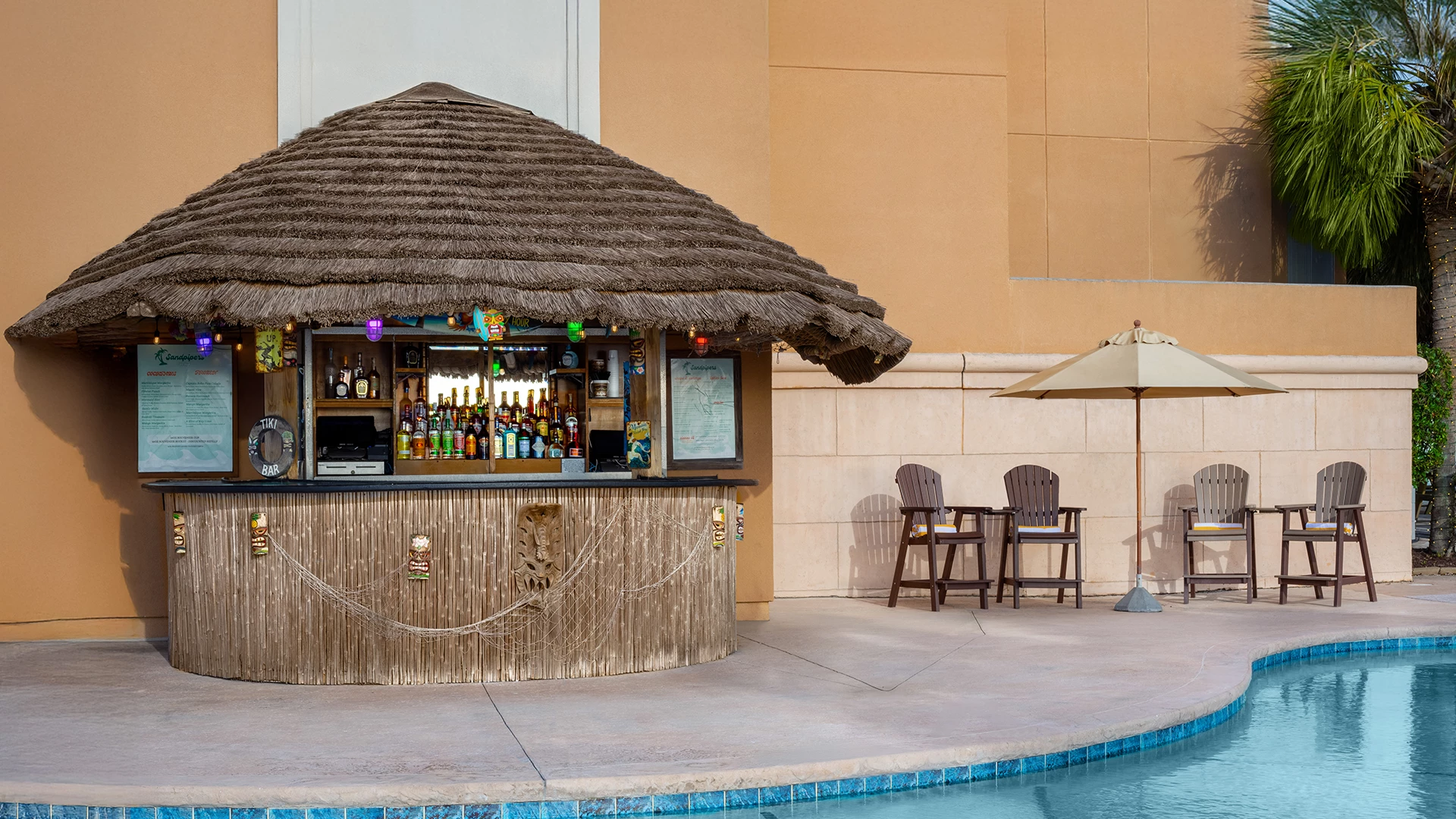 a bar with a straw roof and chairs next to a pool
