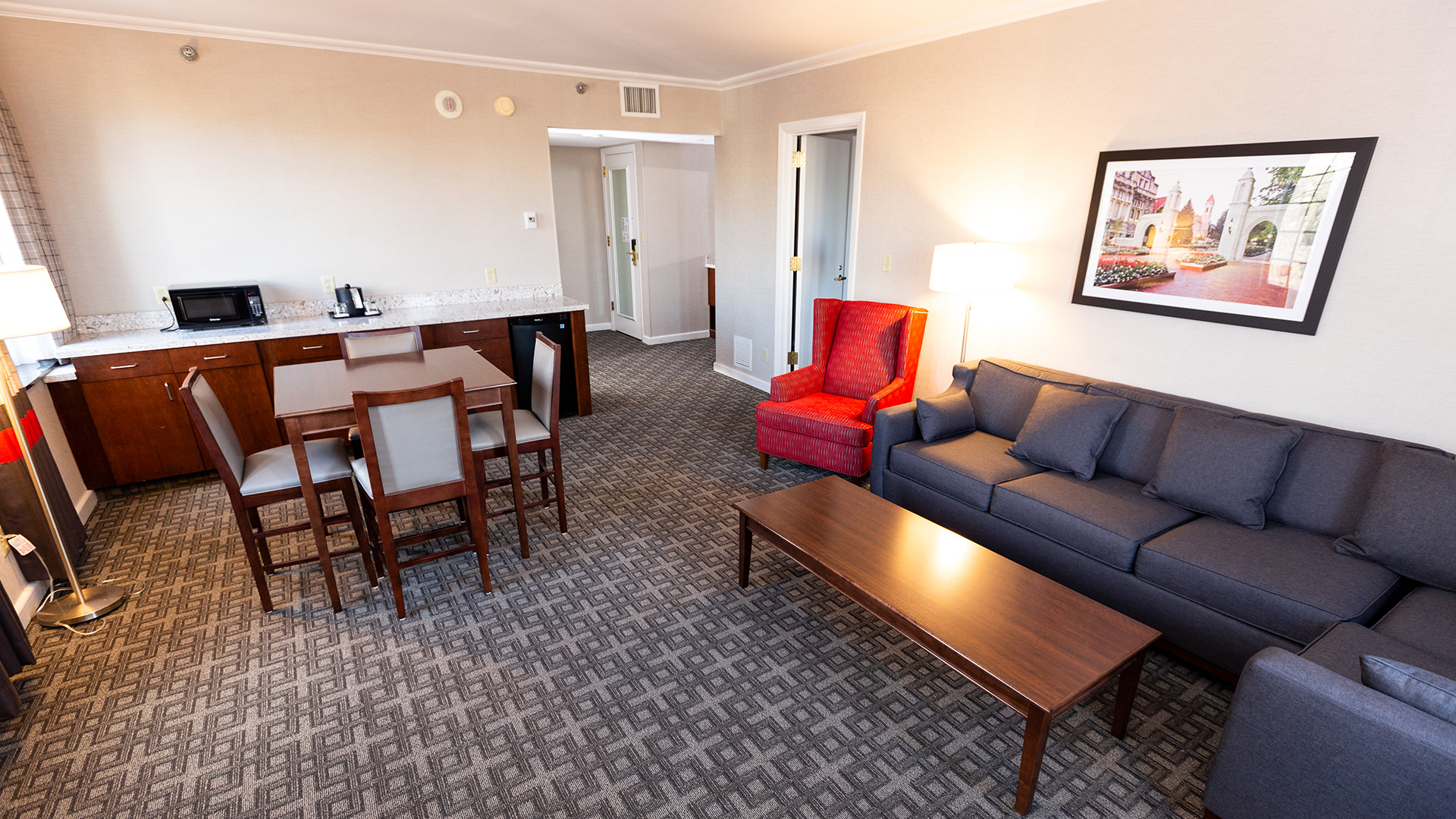 suite living space with a grey sectional sofa, red armchair, dining set, and kitchenette with a microwave