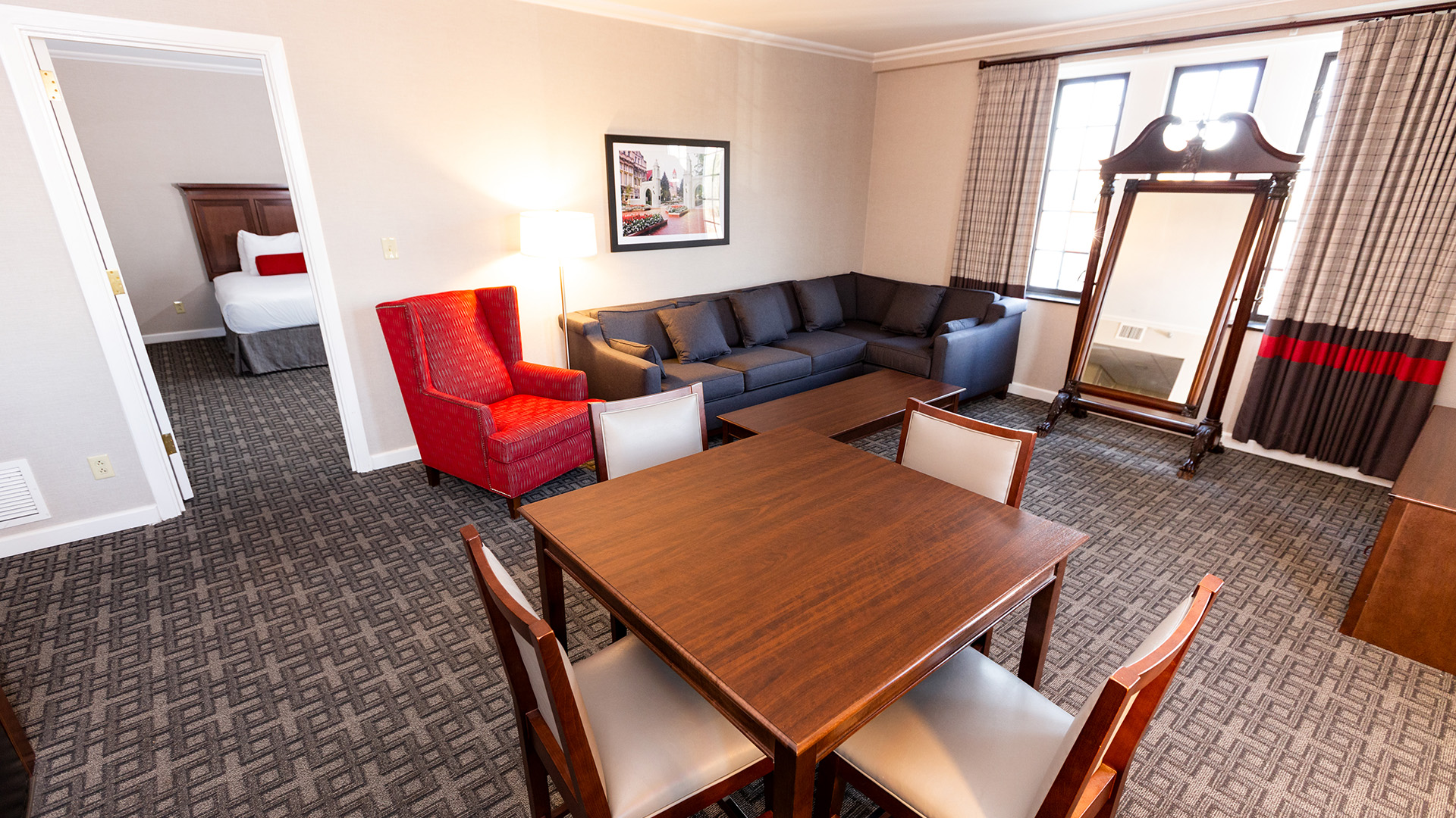 a hotel suite living area featuring a wooden dining table, a red armchair, and a dark grey sectional sofa