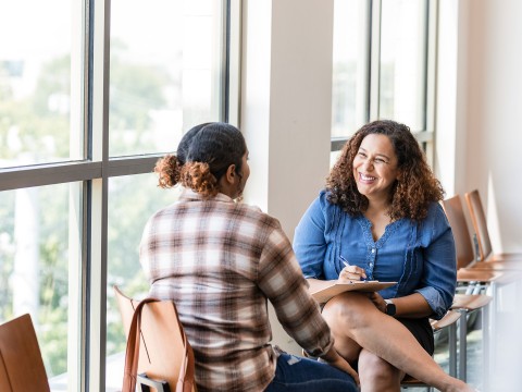 a woman sitting in chairs with a notepad and smiling