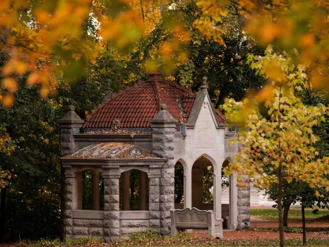 a stone structure with a red roof and a bench in front of trees