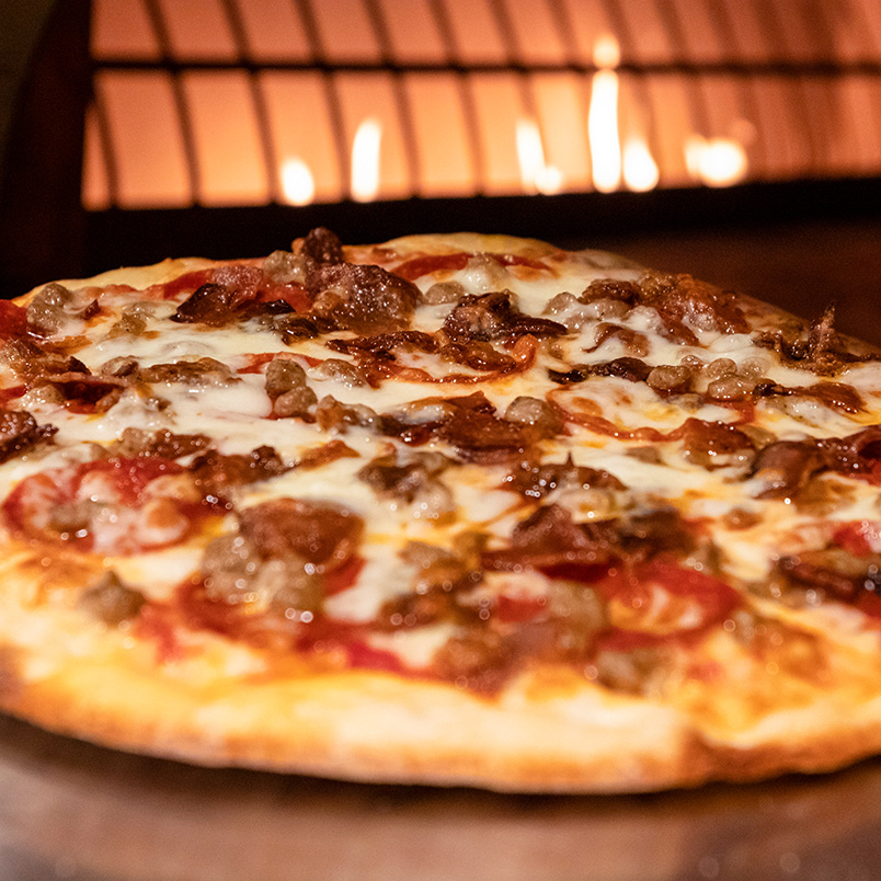 a pizza with meat and cheese on a wood surface