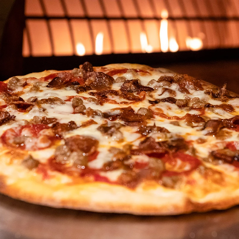 a pizza with meat and cheese on a wood surface