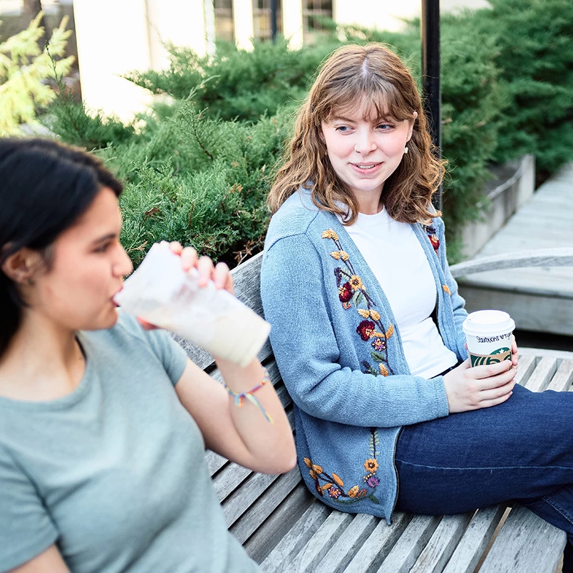 a two women sitting on a bench drinking coffee