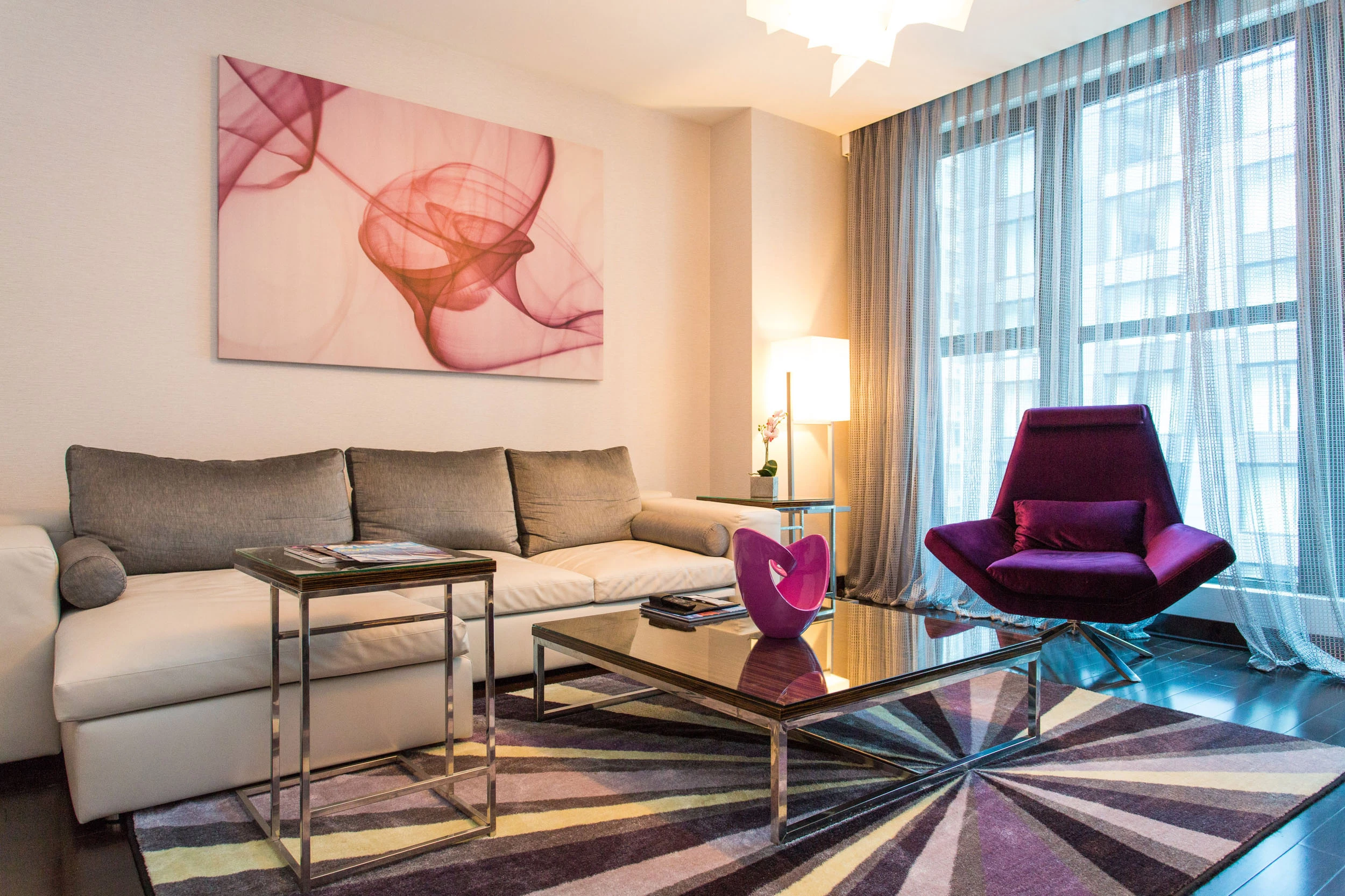 A modern living room with a white sofa, purple armchair, and abstract artwork.