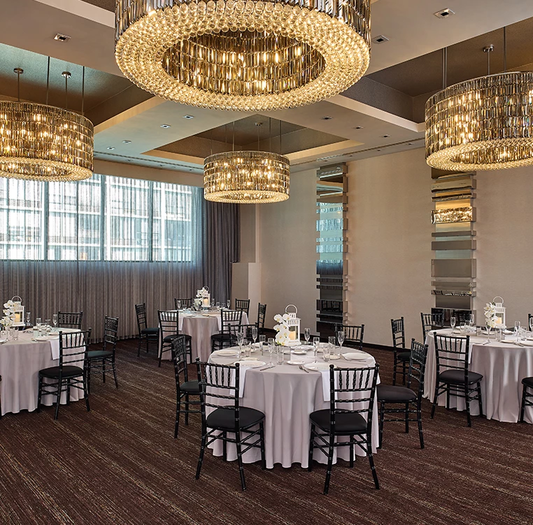 A dining area with round tables, white tablecloths, black chairs, and crystal chandeliers.