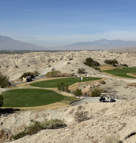 a golf course with sand hills and mountains in the background