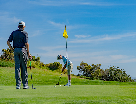 two men playing on the green with a yellow flagstick