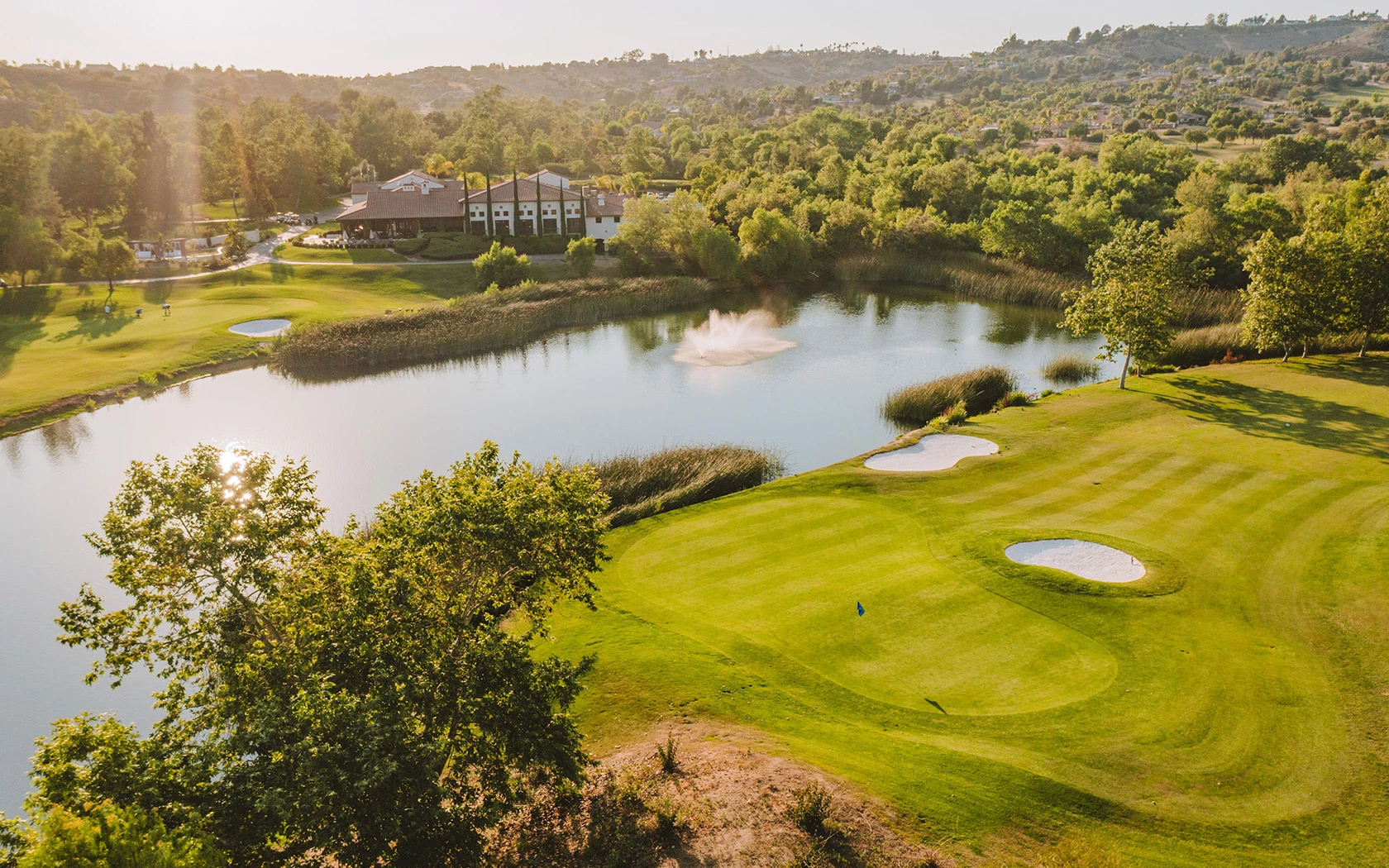 drone shot of a large lake in the middle of the golf course with lots of trees in the distance