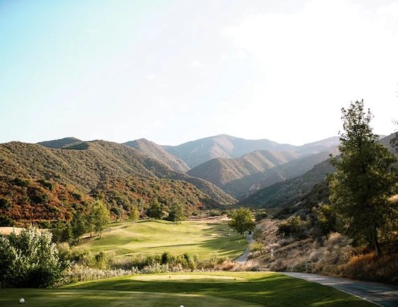 a golf course with trees and mountains in the background