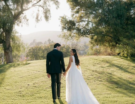a man and woman holding hands and walking on grass