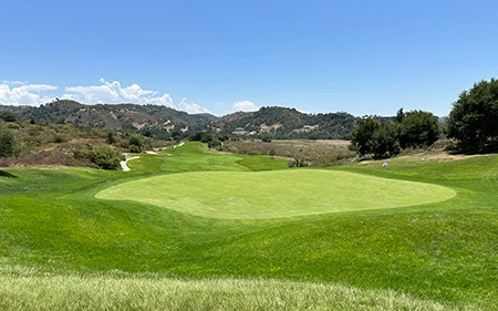 a golf course with a green field and hills in the background
