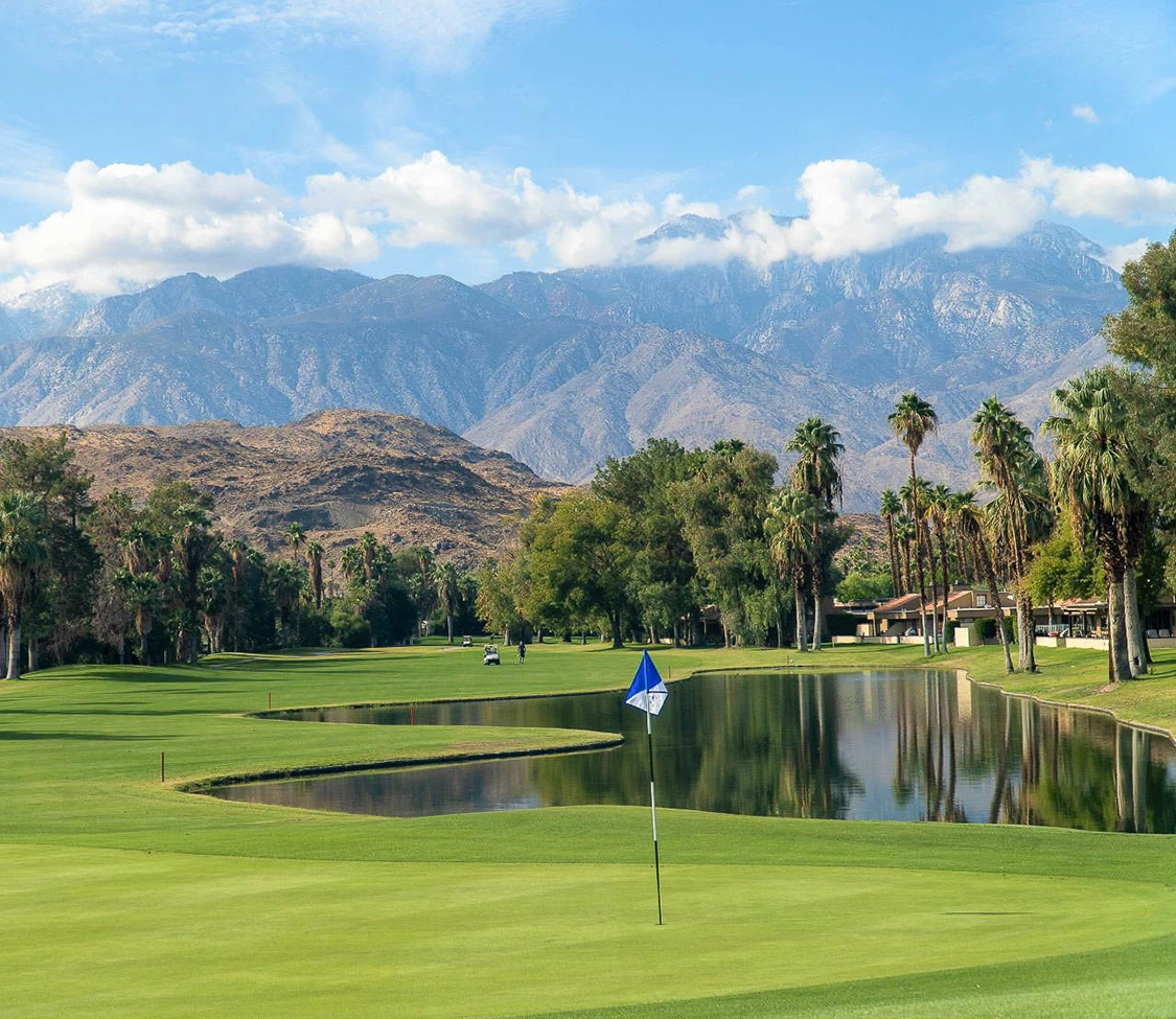 a golf course with a lake and mountains in the background