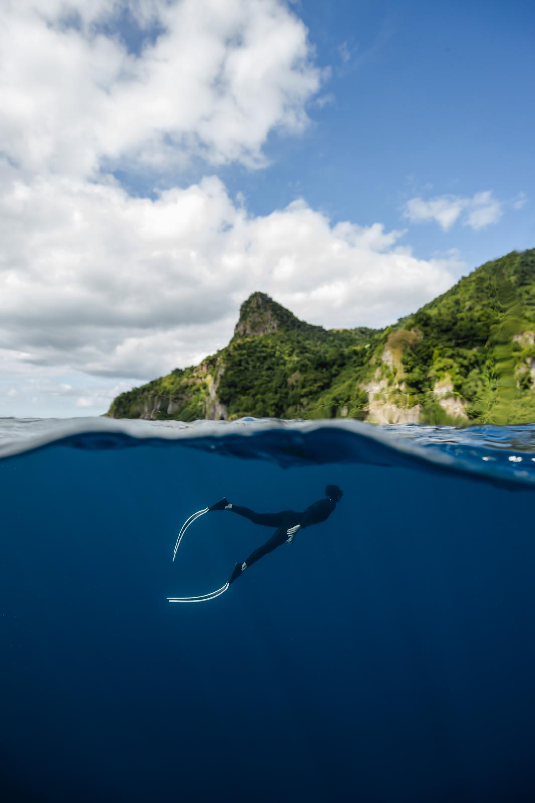 free diver swimming under water with trees and mountains in the background