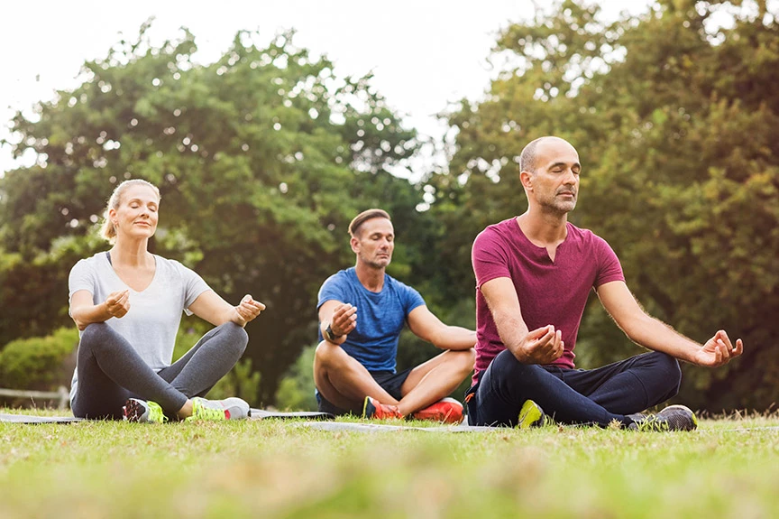 three people doing yoga at a park