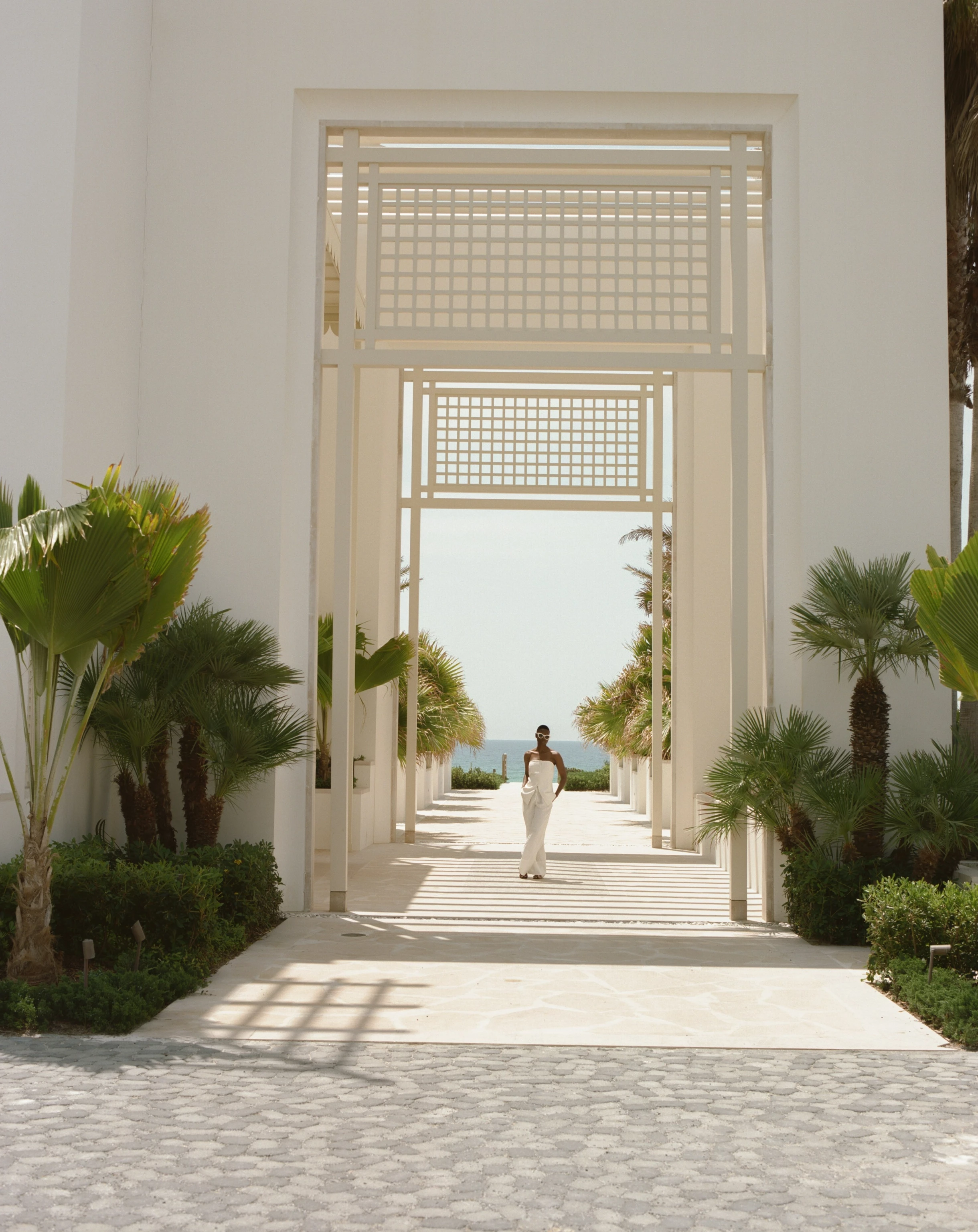 a woman walking down a walkway with palm trees