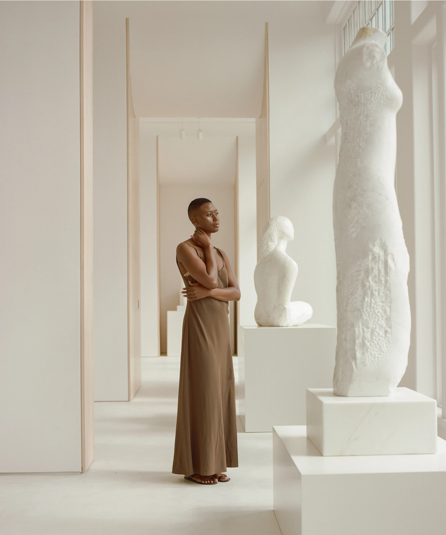 a woman in a brown dress standing in front of a white statue