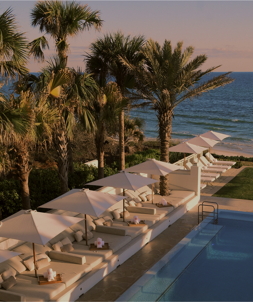 a pool with umbrellas and lounge chairs on the beach