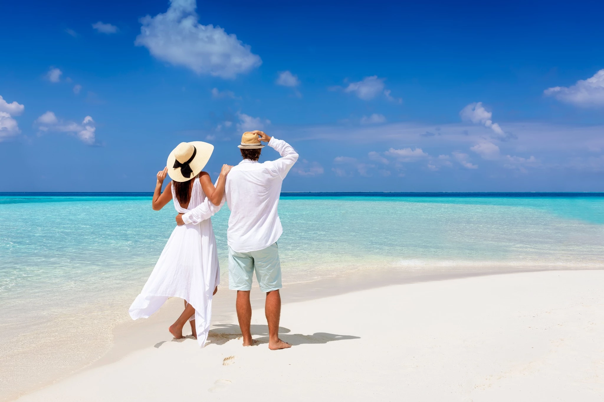 couple in the beach wearing white outfits walking on the shoreline