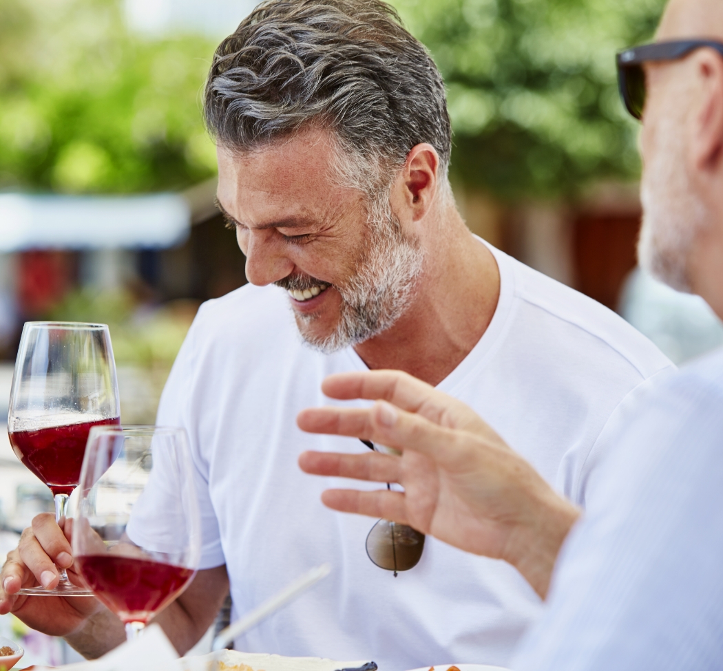 a group of men laughing at a table with wine glasses