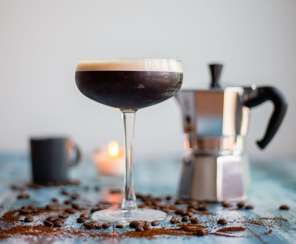 a glass with a drink in it next to coffee beans and coffee maker