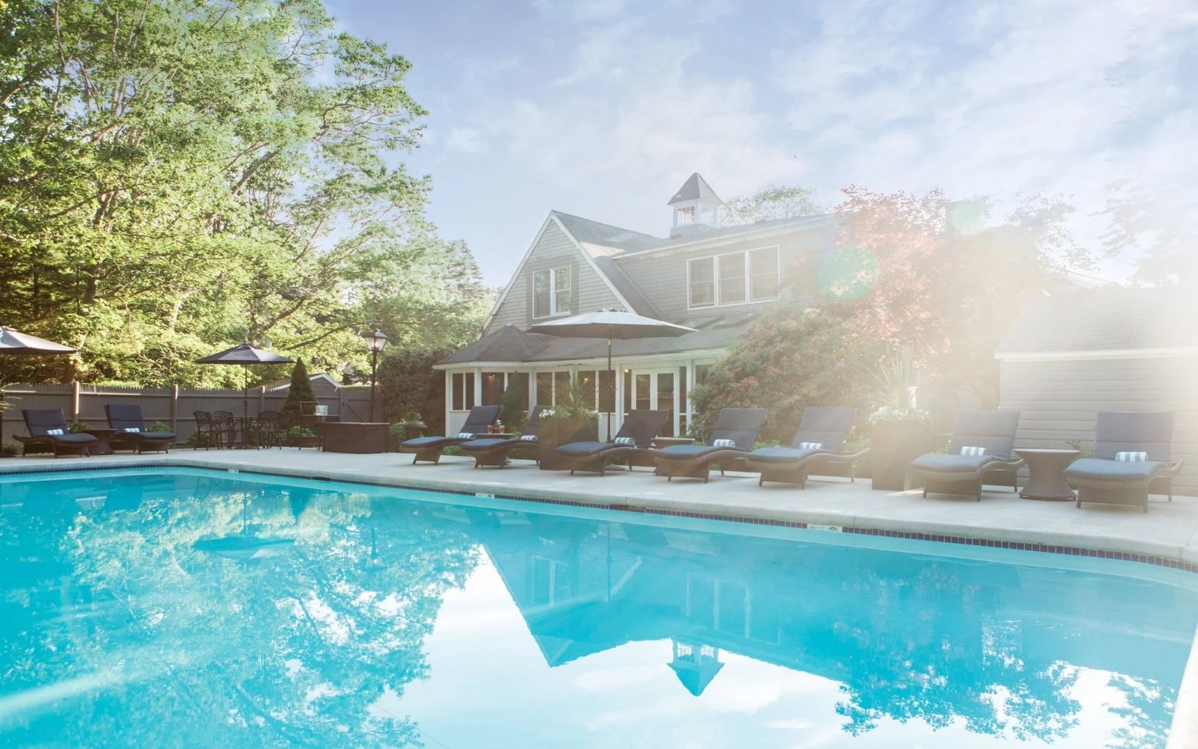 a pool with lounge chairs and umbrellas in front of a house