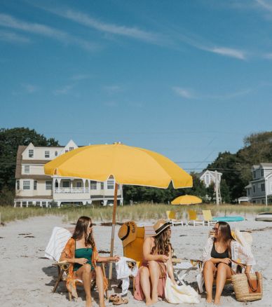 a group of women sitting on a beach with a yellow umbrella