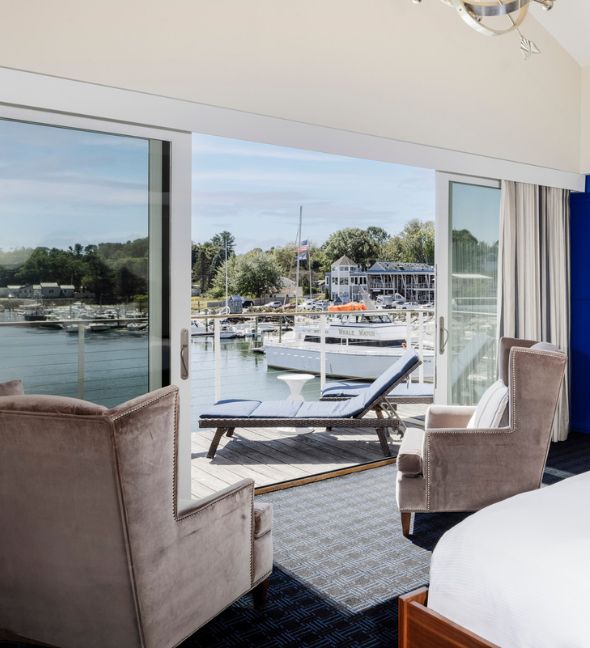 a room with a bed and chairs and a view of the water from the window