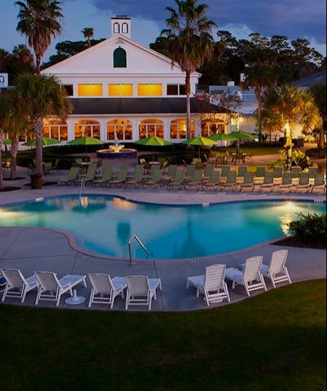 Aerial swimming pool view of the property with pool chairs around at night