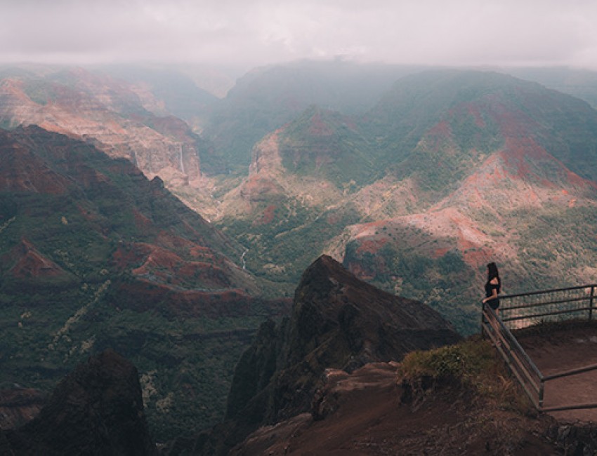 view of the large mountain range on a cloudy day and a woman viewing from an overlook