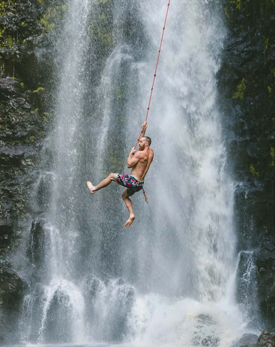 a man from a rope in front of a waterfall
