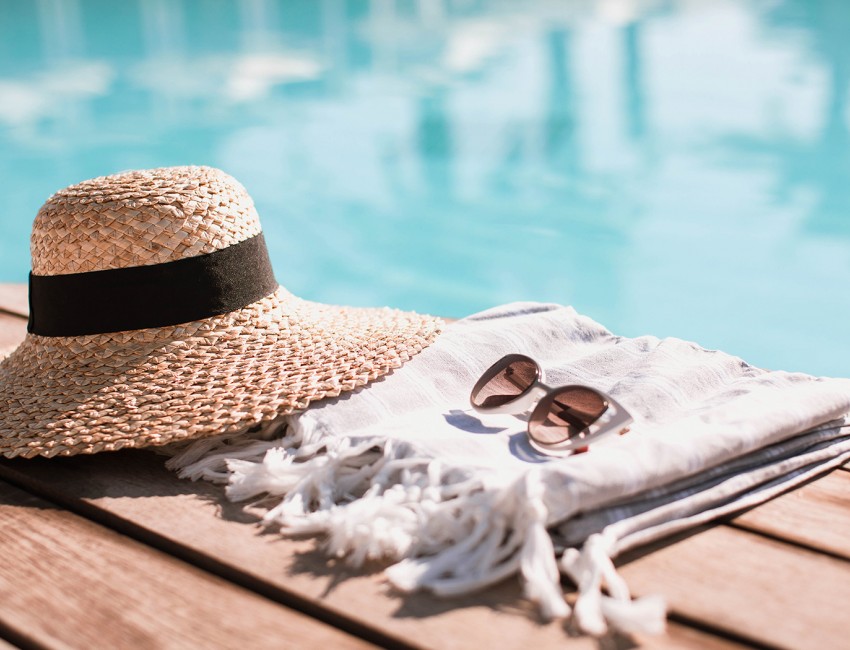 a close up of a straw hat, sunglasses, and a beach towel next to a pool during the day