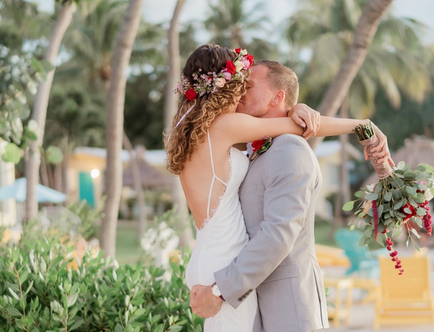 a bride and groom kissing on the beach with palm trees in the background