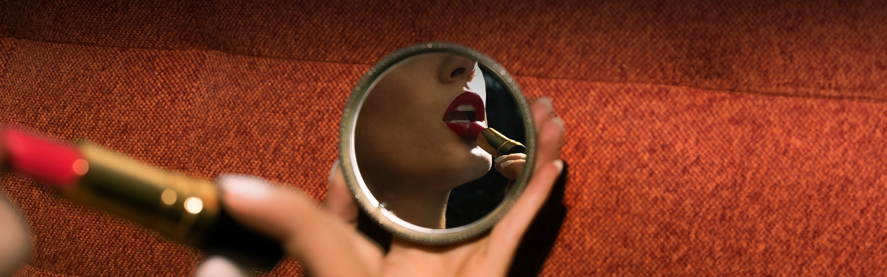 a woman applying lipstick whilst holding a compact mirror
