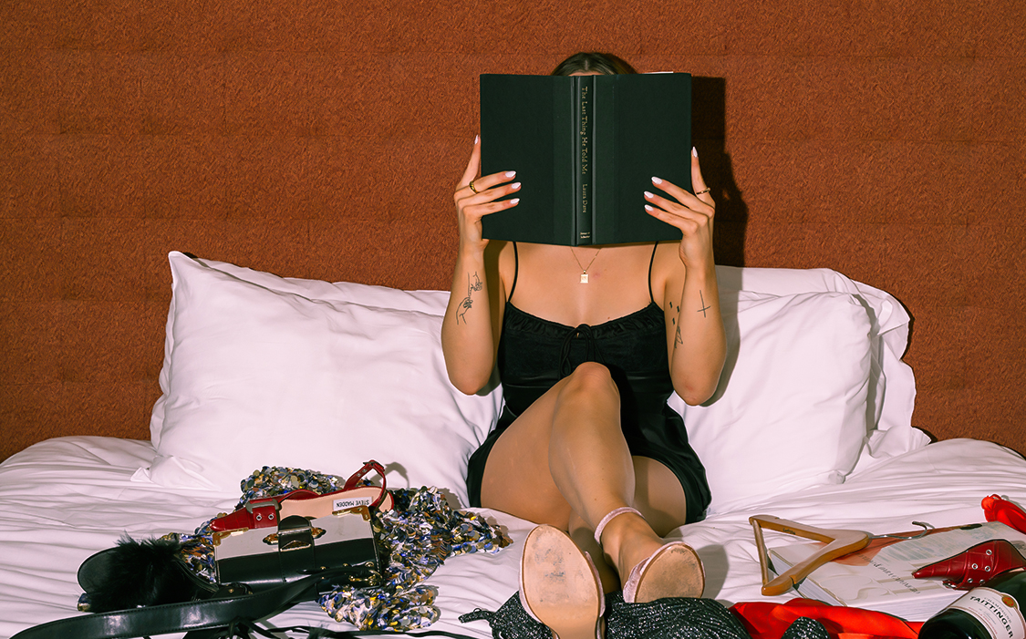 a woman sitting on a bed with a book over her face