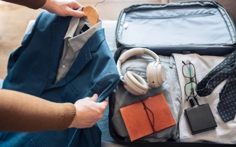 a person packing headphones and other items in a suitcase