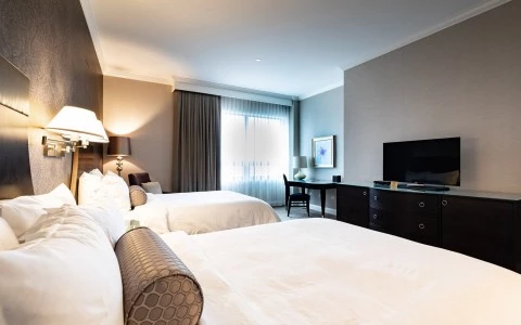 a room with two beds, a flat panel television, and a desk