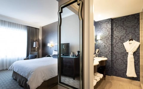 a room with a large mirror and a bathroom with a robe hanging on the wall