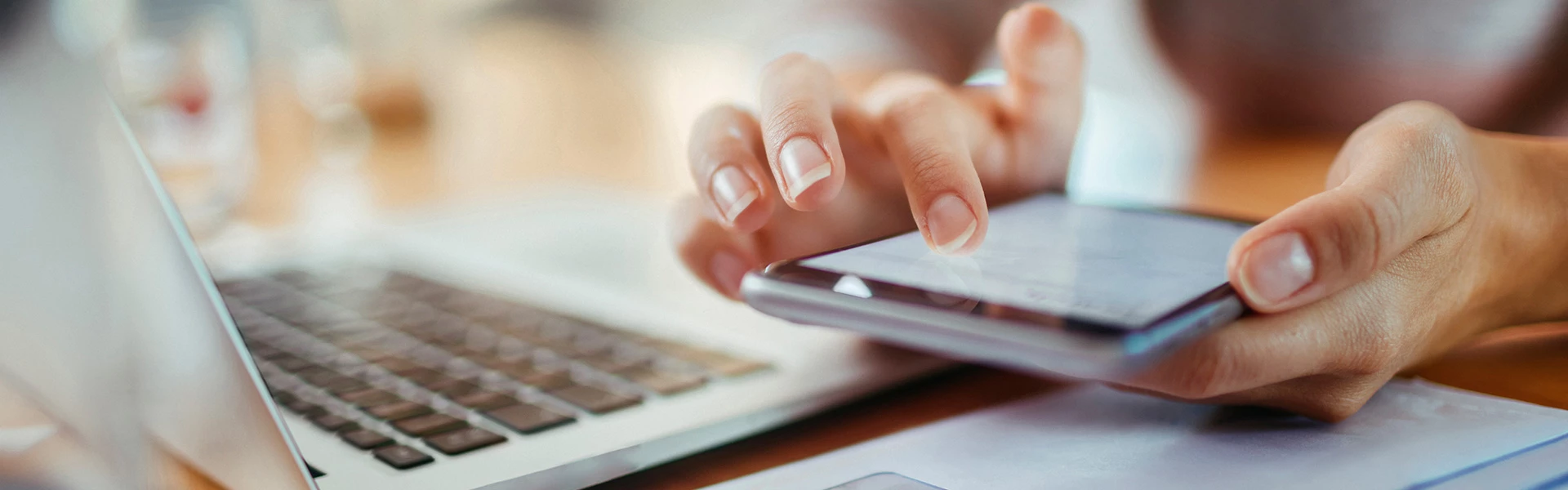 hand scrolling through phone with laptop on desk